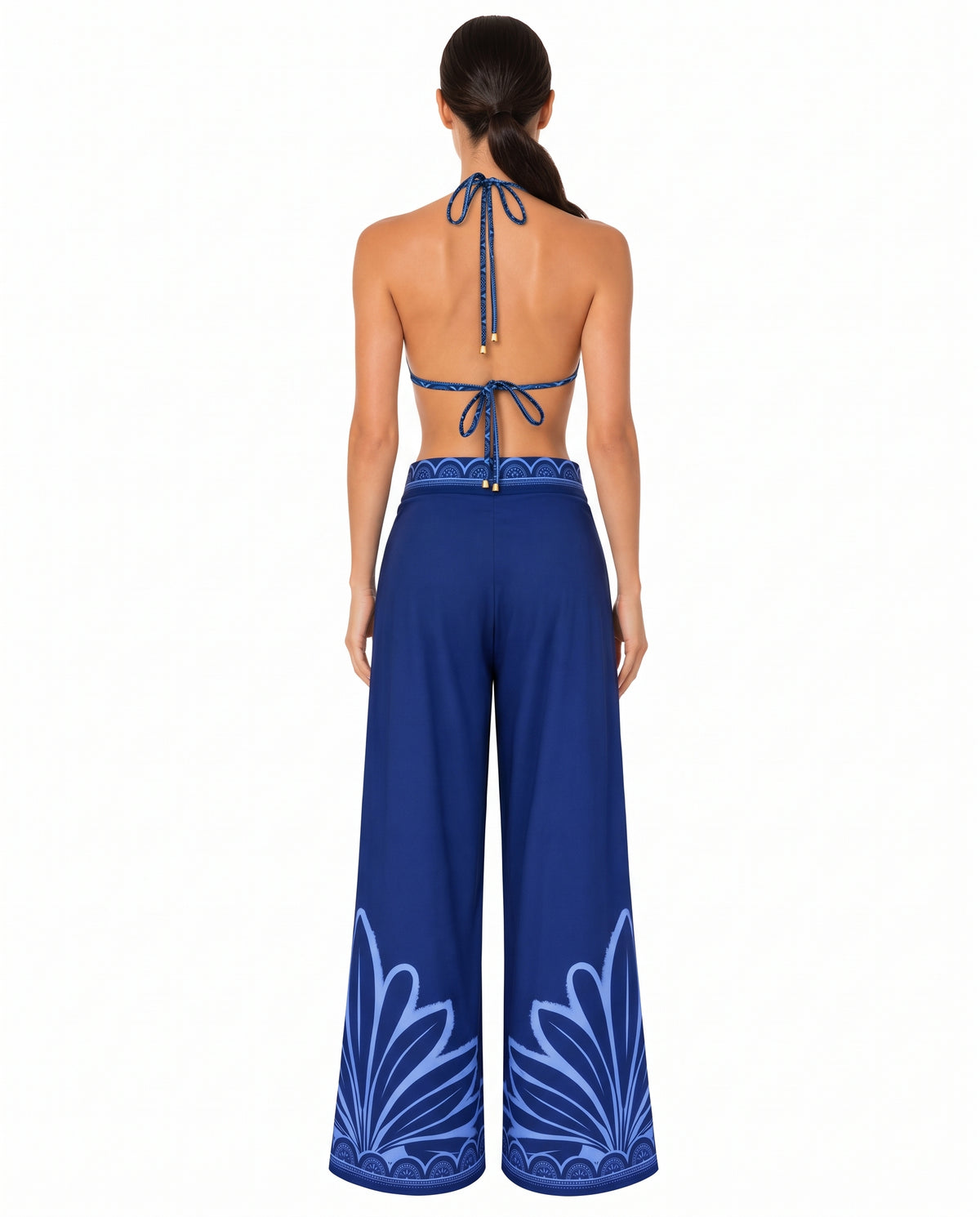 Vista de espalda de un pantalón de seda azul de bota ancha con estampado decorativo celeste en el ruedo y pretina ajustada.